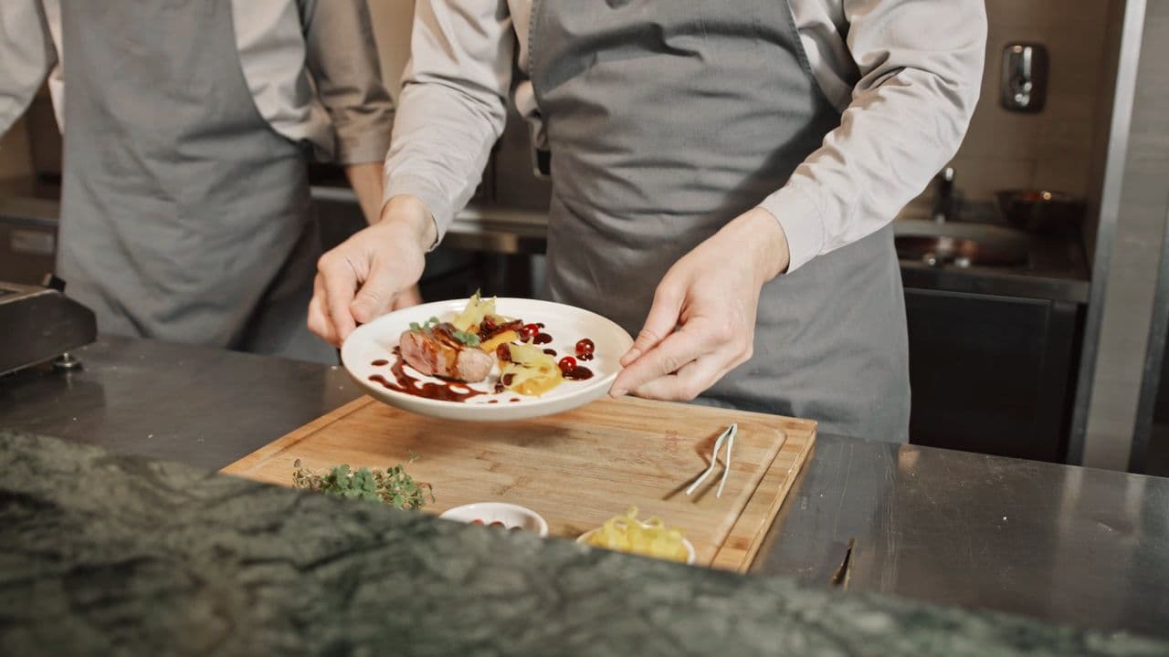 Chefs' hands presenting a beautifully plated dish at the pass